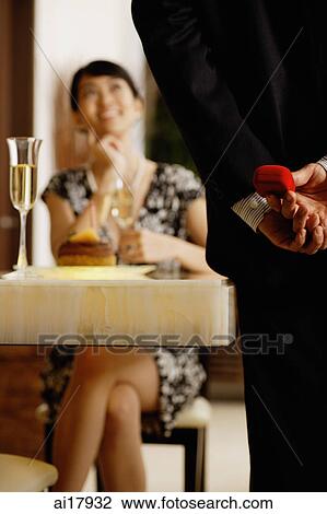 Man standing, holding ring box behind his back, facing seated woman, selective focus View Large Photo Image Stock Image - Man standing, holding ring box behind his back, facing seated woman, selective focus . Fotosearch