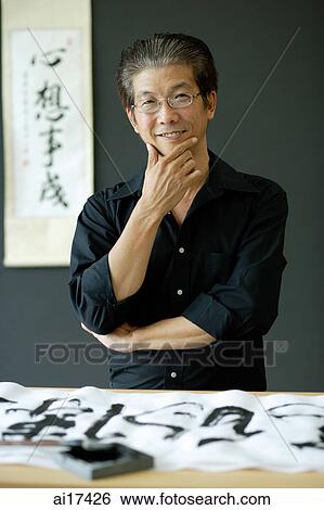 Stock Photograph - Man standing to Chinese brush painting, hand on chin, looking at camera . Fotosearch