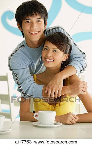 Man with arms around seated woman, smiling at camera View Large Photo Image Stock Image - Man with arms around seated woman, smiling at camera. Fotosearch