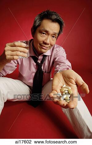 Stock Image - Man with pills in one hand, a glass of water in the other. Fotosearch