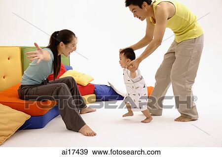 Mother sitting on sofa, arms outstretched, father helping toddler walk towards her View Large Photo Image Stock Photo - Mother sitting on sofa, arms outstretched, father helping toddler walk towards her . Fotosearch
