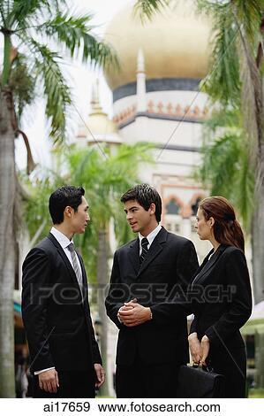 Two businessmen and one businesswoman standing, having a discussion, mosque in the background View Large Photo Image Stock Photo - Two businessmen and one businesswoman standing, having a discussion, mosque in the background . Fotosearch