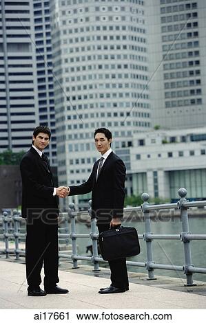 Two businessmen shaking hands, looking at camera, river and buildings in the background View Large Photo Image Stock Image - Two businessmen shaking hands, looking at camera, river and buildings in the background . Fotosearch