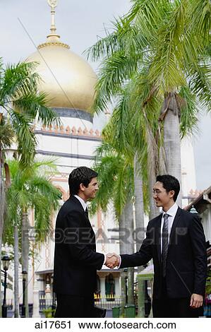 Stock Image - Two businessmen shaking hands, Mosque in the background . Fotosearch