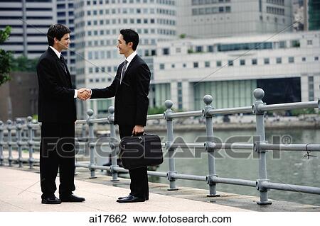 Two businessmen shaking hands, buildings in the background View Large Photo Image Stock Image - Two businessmen shaking hands, buildings in the background . Fotosearch