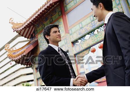 Two businessmen shaking hands, temple gate in the background View Large Photo Image Stock Photo - Two businessmen shaking hands, temple gate in the background . Fotosearch