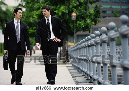 Two businessmen walking side by side, talking View Large Photo Image Stock Photograph - Two businessmen walking side by side, talking. Fotosearch