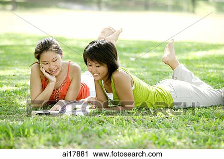 Two young women lying on grass, looking at magazine View Large Photo Image Stock Image - Two young women lying on grass, looking at magazine. Fotosearch