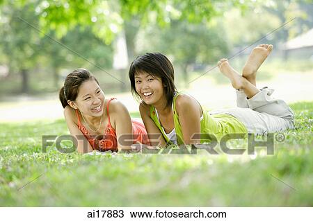 Stock Image - Two young women lying on grass, looking at camera . Fotosearch