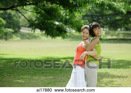 Stock Image - Two young women standing back to back, arm in arm . Fotosearch