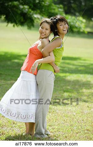 Two young women standing back to back, arm in arm View Large Photo Image Stock Photograph - Two young women standing back to back, arm in arm . Fotosearch