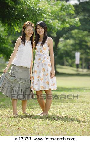 Stock Image - Two young women standing side by side, looking at camera . Fotosearch