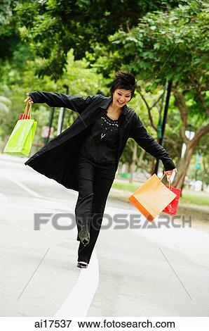 Stock Photo - Woman dressed in black, holding shopping bags, walking on road. Fotosearch