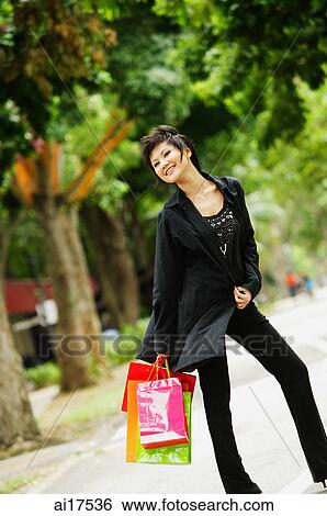 Woman dressed in black, holding shopping bags, smiling View Large Photo Image Stock Photograph - Woman dressed in black, holding shopping bags, smiling. Fotosearch