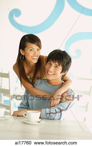 Stock Image - Woman embracing seated man, both smiling at camera. Fotosearch