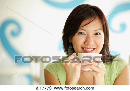 Stock Image - Woman holding cup, smiling at camera. Fotosearch