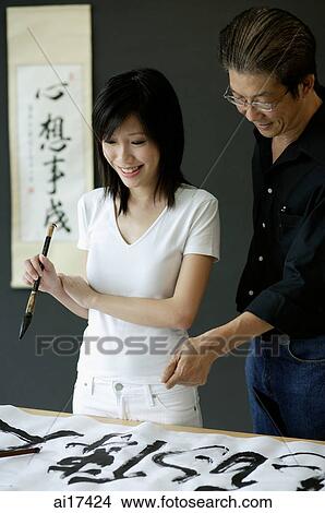 Woman holding paintbrush, looking at Chinese painting, man standing next to her View Large Photo Image Picture - Woman holding paintbrush, looking at Chinese painting, man standing next to her . Fotosearch