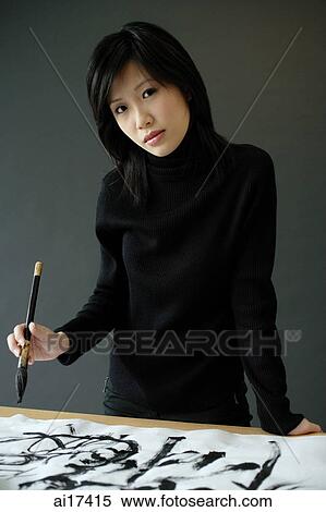 Woman holding paintbrush, standing next to table with Chinese calligraphy on it, looking at camera View Large Photo Image Stock Photography - Woman holding paintbrush, standing next to table with Chinese calligraphy on it, looking at camera . Fotosearch