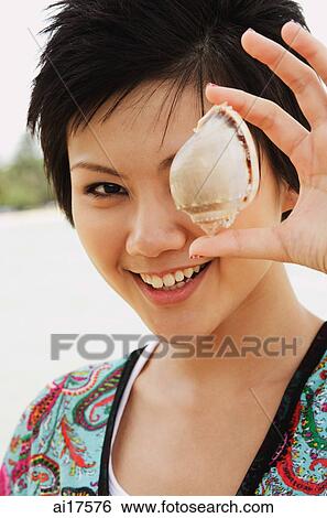 Woman holding shell over one eye, smiling at camera View Large Photo Image Stock Photograph - Woman holding shell over one eye, smiling at camera. Fotosearch