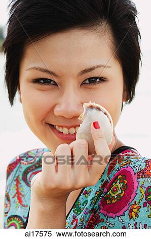 Stock Photography - Woman holding shell, smiling at camera, portrait . Fotosearch