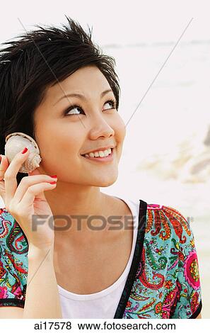 Woman holding shell to ear, looking away View Large Photo Image Stock Photo - Woman holding shell to ear, looking away . Fotosearch