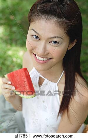 Stock Image - Woman holding slice of watermelon, smiling at camera . Fotosearch