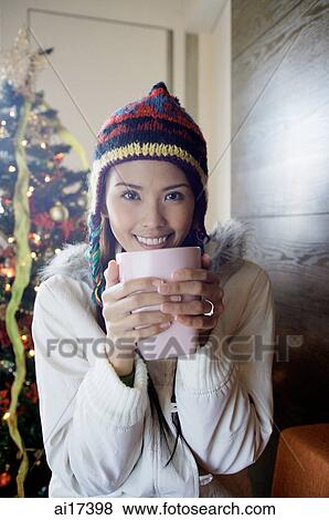 Stock Photo - Woman in jacket and cap, holding mug in both hands . Fotosearch