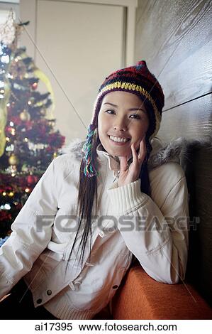 Woman in jacket and cap, smiling at camera, Christmas tree behind her View Large Photo Image Stock Photography - Woman in jacket and cap, smiling at camera, Christmas tree behind her . Fotosearch