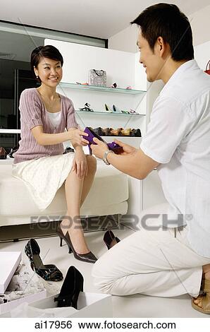 Stock Photograph - Woman in shoe shop, trying on shoes, man kneeling in front of her handing her a shoe. Fotosearch