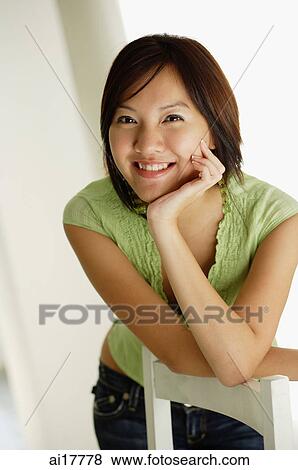Woman leaning on back of chair smiling at camera View Large Photo Image Stock Photo - Woman leaning on back of chair smiling at camera . Fotosearch
