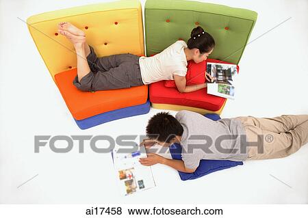 Woman lying on sofa reading a magazine, man lying on floor reading magazine View Large Photo Image Stock Photo - Woman lying on sofa reading a magazine, man lying on floor reading magazine . Fotosearch