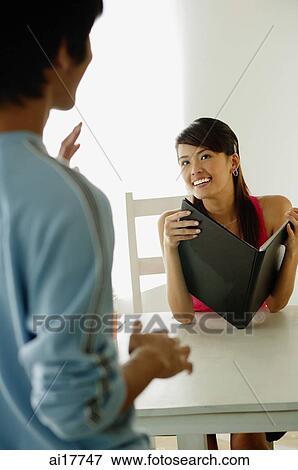 Woman sitting at cafe table, holding menu, looking at man standing in front of her View Large Photo Image Stock Photo - Woman sitting at cafe table, holding menu, looking at man standing in front of her . Fotosearch