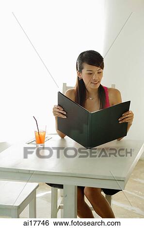 Stock Photograph - Woman sitting at cafe table, holding menu . Fotosearch