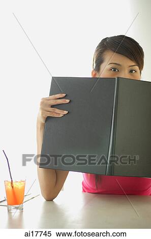 Woman sitting at cafe table, holding menu over her face View Large Photo Image Stock Photography - Woman sitting at cafe table, holding menu over her face . Fotosearch