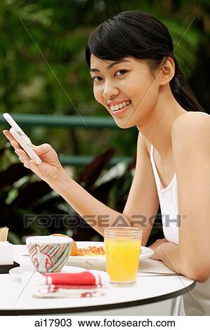 Woman sitting at table, holding mobile phone View Large Photo Image Stock Image - Woman sitting at table, holding mobile phone . Fotosearch