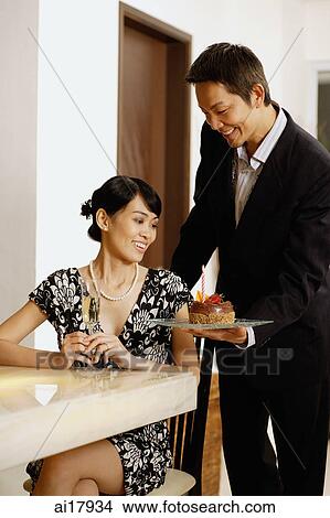 Woman sitting at table, man serving her a cake View Large Photo Image Picture - Woman sitting at table, man serving her a cake . Fotosearch