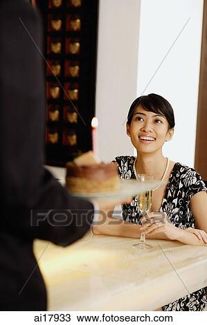 Woman sitting at table with Champagne glass, man serving her a cake View Large Photo Image Stock Image - Woman sitting at table with Champagne glass, man serving her a cake . Fotosearch