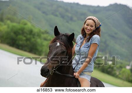 Stock Image - Woman sitting on horse, smiling at camera . Fotosearch