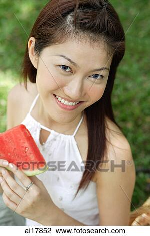 Stock Image - Woman with slice of watermelon, smiling at camera . Fotosearch