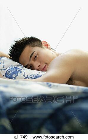 Young man lying on bed, looking at camera View Large Photo Image Stock Image - Young man lying on bed, looking at camera . Fotosearch