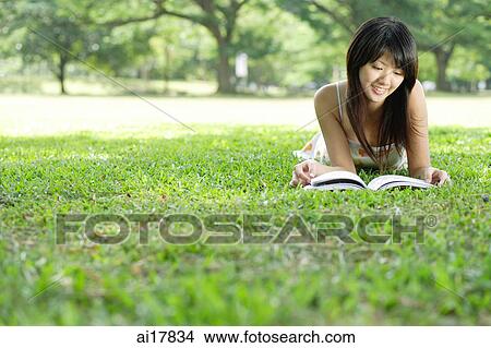 Young woman lying on grass in park, looking at magazine View Large Photo Image Picture - Young woman lying on grass in park, looking at magazine . Fotosearch