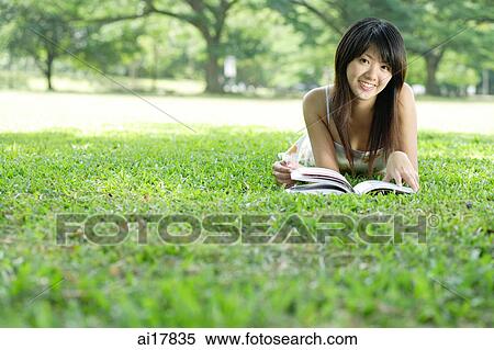 Young woman lying on grass in park, looking at camera View Large Photo Image Stock Photography - Young woman lying on grass in park, looking at camera. Fotosearch
