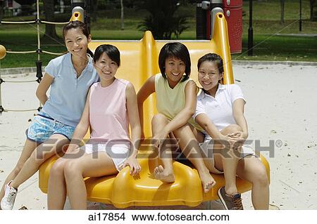 Young women sitting on slide in playground, smiling at camera View Large Photo Image Picture - Young women sitting on slide in playground, smiling at camera . Fotosearch