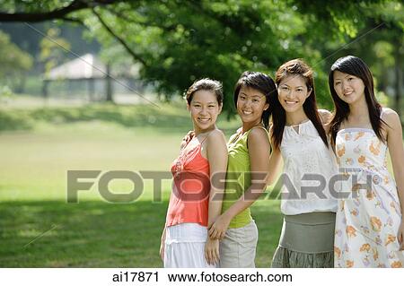 Stock Image - Young women standing side by side, smiling at camera. Fotosearch
