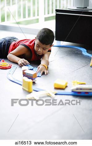 Boy lying on floor, playing with toy train View Large Photo Image Stock Image - Boy lying on floor, playing with toy train . Fotosearch
