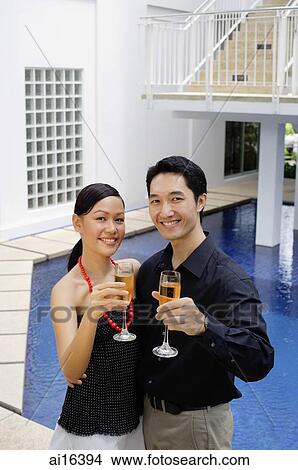 Couple by poolside, holding up champagne glasses towards camera View Large Photo Image Picture - Couple by poolside, holding up champagne glasses towards camera. Fotosearch
