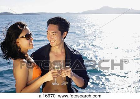 Couple holding champagne glasses, toasting, ocean behind them View Large Photo Image Stock Image - Couple holding champagne glasses, toasting, ocean behind them . Fotosearch