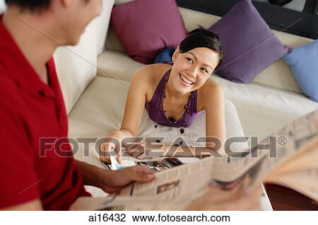 Stock Image - Couple in living room, reading . Fotosearch