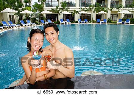 Couple in swimming pool, holding cocktails, smiling at camera View Large Photo Image Stock Image - Couple in swimming pool, holding cocktails, smiling at camera . Fotosearch