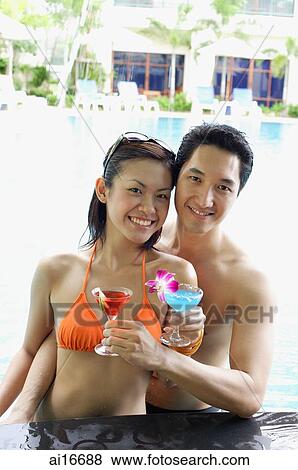 Couple in swimming pool holding cocktail drinks, smiling at camera View Large Photo Image Stock Photo - Couple in swimming pool holding cocktail drinks, smiling at camera . Fotosearch
